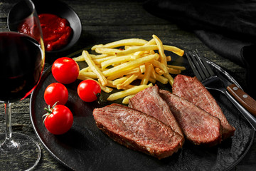 Medium rare sirloin steak with chips and red wine on a rustic wooden table. Classic European lunch. Closeup shot.