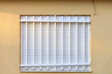 White metal shutters on the window of the facade of the house are closed with a white metal grill.