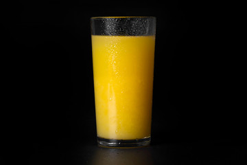 A glass of fresh orange juice on a black background, close-up.