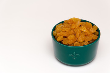 White or golden raisins in a blue ceramic bowl on a white background. Healthy eating concept. Closeup. Copy space