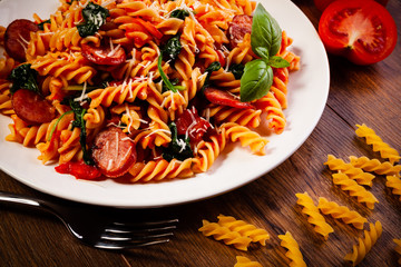 Fusilli with sausages and vegetables on wooden table