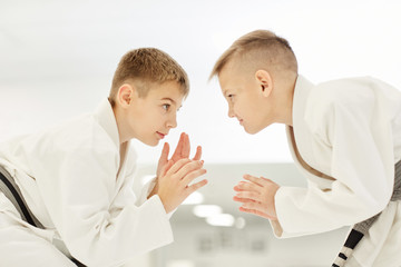 Two little boys in kimono standing opposite each other and practicing strikes in karate