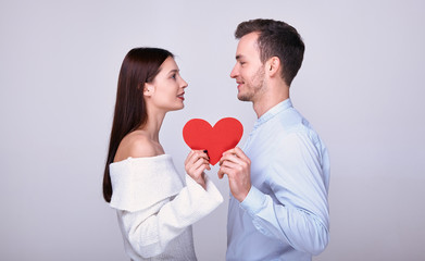 The couple look at each other and hold a red paper heart.
