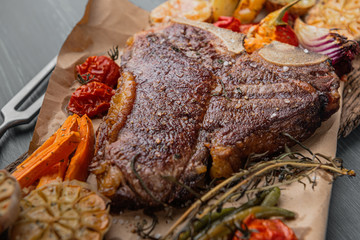 tender and juicy steak on the bone grilled next to baked and grilled vegetables, the concept of tasty and healthy nutrition