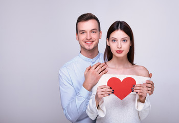 Nice smiling guy hugs beautiful girl who is holdingred cardboard heart