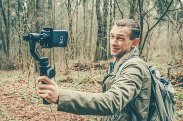 male blogger films himself in the woods on a mobile phone camera and gimbal, smiling and waving at the camera. The concept of blogging, Internet, information