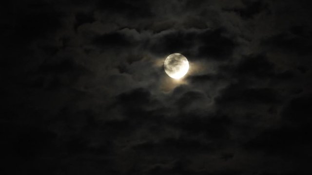 Full moon at night with cloud real time. 4k video full moon in the black sky.  Clouds passing by moon at night. night sky with cloudy weather