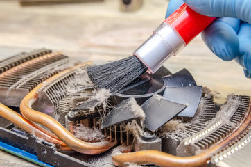 man's hand in blue gloves with a brush cleans the cooler of the video card close-up. Dust on the...