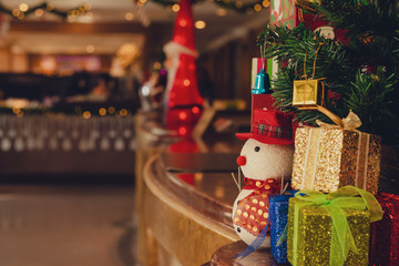 Snowman wearing a red hat with gift boxes and Christmas tree decorations in a warm house ready to welcome the upcoming Christmas holidays, Selective focus, Vintage style.