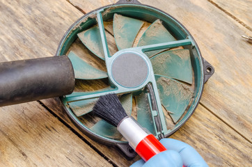 Cleaning the dusty green cooler from the computer with a brush and vacuum cleaner on a wooden table close-up. concept of scrapers parts of the computer
