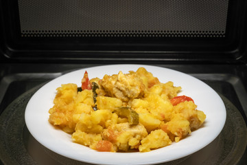 Cooking, heating food in the microwave. Baked potatoes with meat, vegetables on a white plate in the microwave top view.