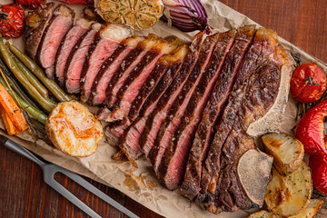 marbled beef steak on the bone cooked to a state of medium rare grill. next to the steak, grilled vegetables serving as a side dish. lovely gala dinner for two