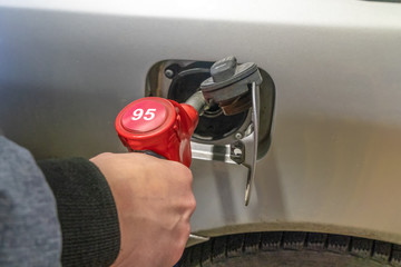 man's hand refuels a gray car at a gas station close up