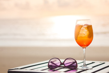 Delicious iced aperol spritz served on a small wooden table on a hot tropical beach in summer sunshine