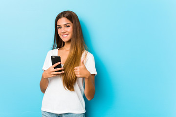 Young caucasian woman holding a phone smiling and raising thumb up