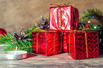 Red mini-gifts on a wooden background among fir branches, candles, cones. Beautiful Christmas background.