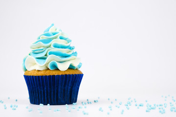 Cupcake on birthday with blue and white cream on white background, decorated with sprinkles.