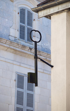 A cast iron key is mounted on a wall against the backdrop of houses with blue shutters on the windows in a small town
