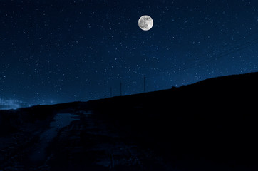 Naklejka na ściany i meble Long exposure shot. Mountain Road through the forest on a full moon night. Scenic night landscape of dark blue sky with moon. Azerbaijan