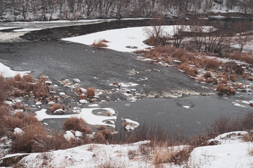 First snow fell on dry grass on banks of river.