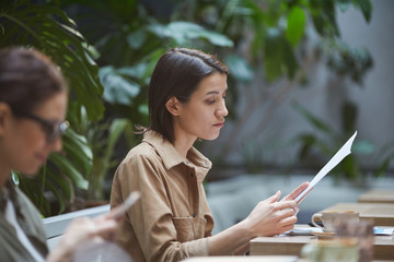 Side view portrait of young businesswoman reading documents while working in outdoor cafe, copy...