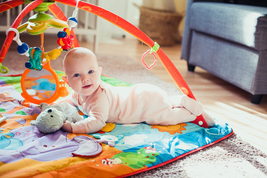 4 months old baby girl lying on colorful play mat on the floor. Activity carpet for kids.