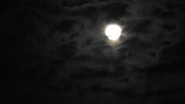 Full moon at night with cloud real time. 4k video full moon in the black sky.  Clouds passing by moon at night. night sky with cloudy weather
