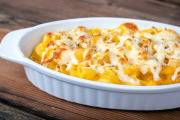 Butternut squash mac and cheese dish closeup on a rustic table and grated cheese on top