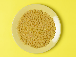 dry pasta laid out on a yellow plate which stands on a yellow background. The view from the top