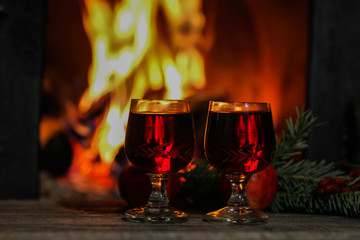 Two glasses of red wine against a roaring fire