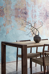 Stylish interior design of dining room in loft apartment with wooden sharing table, chairs,flowers in vase and elegant accessories. Modern home decor. Bright and sunny industrial space. Template.