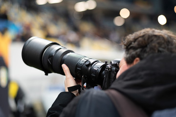 A professional photographer with a professional camera shoots a football match at the stadium - obrazy, fototapety, plakaty