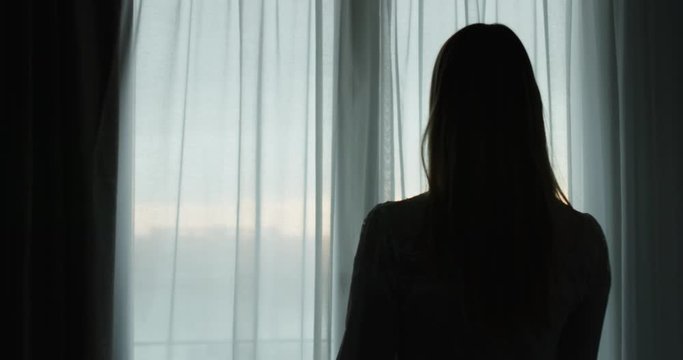 Close up back view of an young woman is opening a curtain of a window in a hotel during her vacation in a morning.