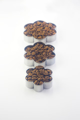  molds of different sizes in the form of a flower filled with coffee beans standing next to each other on a white background
