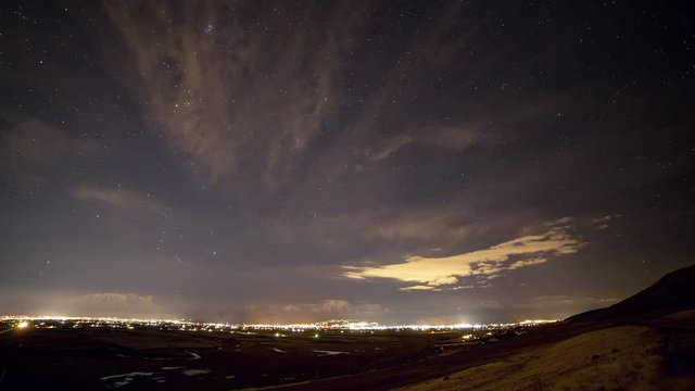 Time lapse of the nights sky over city lights as stars move overhead and cars drive in the foreground.