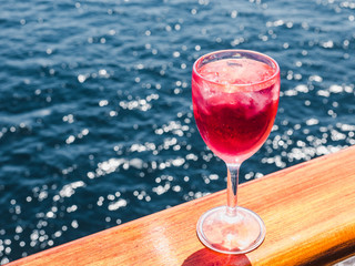 Beautiful glass of pink wine on the open deck of a cruise liner against the backdrop of blue sea waves. Side view, close-up. Concept of leisure and travel