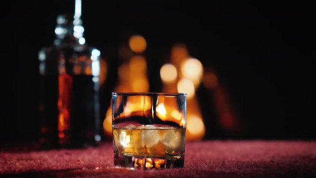 Glass with strong alcohol and a bottle on the background of the fireplace