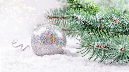 Fototapeta na wymiar Silver round Christmas and New Year bauble on the white snow background and branches of blue natural fir. Greeting card, symbol of Christmas and New Year.