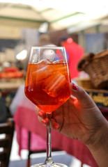 Woman holding a glass of Aperol Spritz on a restaurant table in Italy