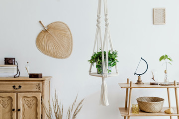 Stylish and minimalistic boho interior with design and handmade macrame shelf planter hanger for indoor plants, wooden furnitures, elegant accessories ,rattan basket and leaf. Cozy home decor.