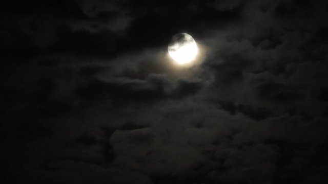 Full moon at night with cloud real time. 4k video full moon in the black sky.  Clouds passing by moon at night. night sky with cloudy weather
