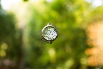 dead line time concept picture of falling hand clock in air on blurred bokeh outdoor natural colorful wallpaper pattern background space 