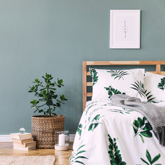 Minimalistic composition of bedroom interior with wooden bed, mock up poster frame, rattan basket, plants, books and elegant accessories. Beautiful bed sheets, blanket and pillow. Template. Home decor