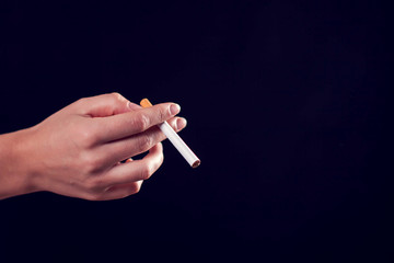 Cigarette in hand on black background. Nicotine addiction concept