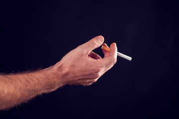 Cigarette in hand on black background. Nicotine addiction concept