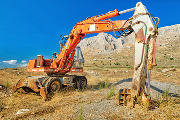 Side view of long arm of excavator in a mine with sand, earth and pebbles around for building work in a suggestive construction site. Work in progress, industrial machine. Blue sky.