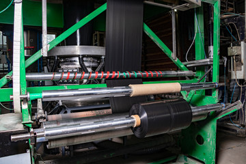 Black plastic trash bags are rolled up. Extruder blows a sleeve of plastic film