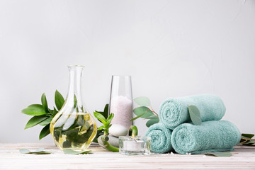 Spa concept. Body oil for massage, pink sea salt, turquoise towels in a roll, eucalyptus, candle, sea stones, bamboo and tropical leaves on a light wooden background. Copy space.