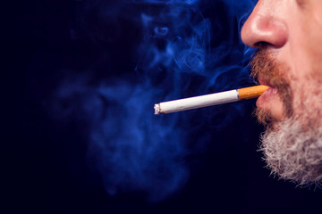 A portrait of the man smokes cigarette on black background. Nicotine addiction concept