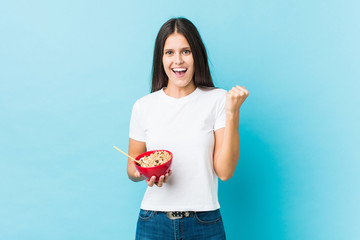 Young caucasian woman holding a cereals bowl cheering carefree and excited. Victory concept.